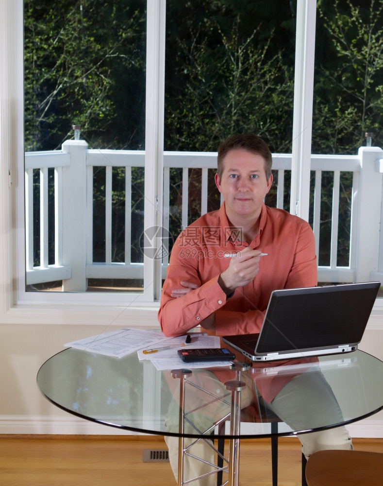 成人男子在家中工作时用笔计算器和纸在桌顶大窗背景上时用笔持往前向看的垂直照片图片