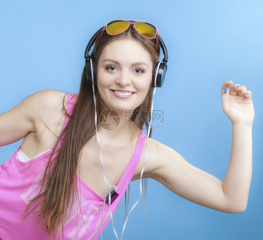 时装少女耳机听音乐mp3播放器新鲜的精力充沛年轻女青放松快乐和舞蓝背景图片