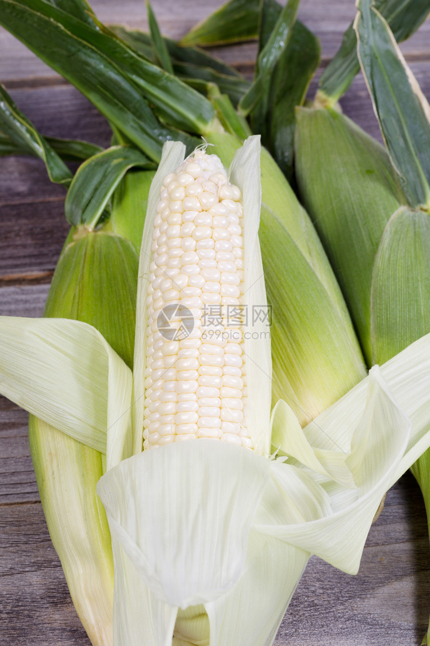 白色甜玉米的垂直视图从尾巴上剥回来在生锈木上背着景的全圆玉米图片