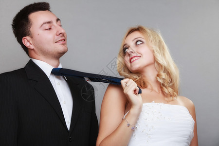 结婚日幸福的已夫妇金新娘和郎的肖像女人拉着男的领带工作室拍着灰色的背景背景图片