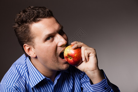 快乐的年轻人在黑暗灰色上吃着咬苹果季节水建议健康营养或牙科护理图片