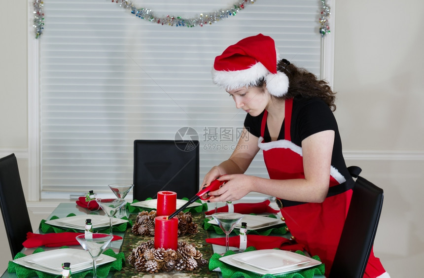 年轻少女身着圣诞老人服装在餐厅桌边为节日晚会点蜡烛图片