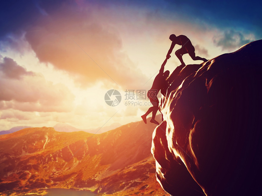 攀爬在岩石上日落时山其中一人伸出手帮助攀爬在危险情况下帮助支持援图片