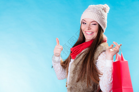 穿着温暖衣服的冬季妇女穿着红色纸袋露出蓝的拇指女孩买东西销售消费主义和零售业背景图片