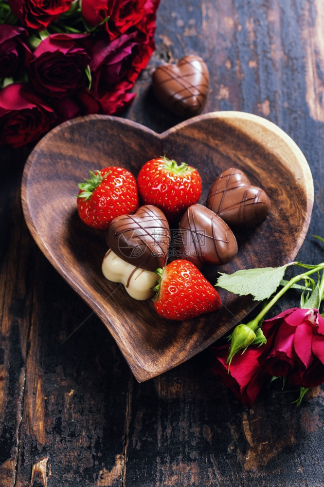 木制桌上有草莓和巧克力的心形板盘情人节和r日与爱的概念图片