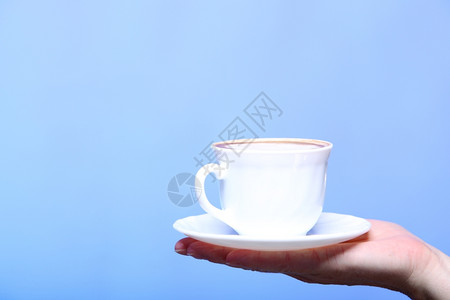 在秋冬时握着一杯拿铁咖啡卡布奇诺热饮的紧女手复制蓝色背景圣诞节高清图片素材