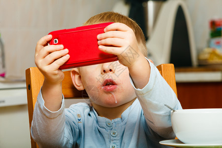 小男孩脏嘴流口水吃早餐在桌上玩手机图片
