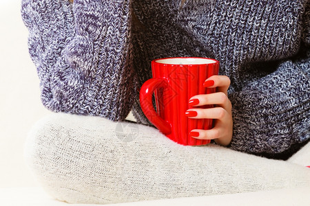 热饮紧女手握着红杯热茶或咖啡坐在沙发上穿着暖和毛衣的妇女自己暖和起来举办高清图片素材