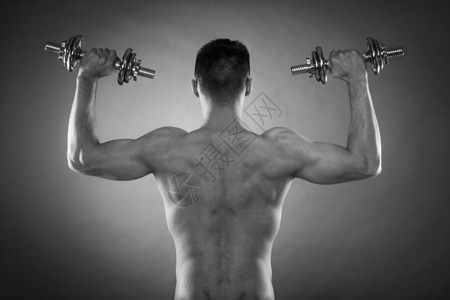 健壮体强壮的人与哑铃一起锻炼运动肌肉健壮的年轻人举起重量的后视暗背景图片