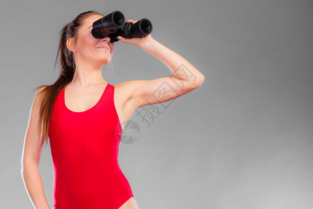 身穿救生警卫服红泳值勤穿双筒望远镜看灰色的有吸引力女模范背景图片