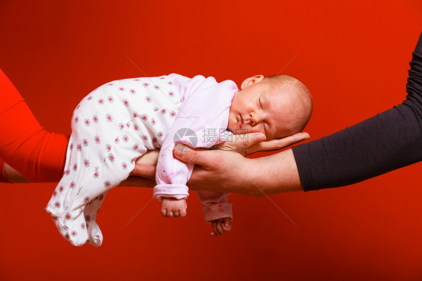一个月大的女婴睡在父母怀抱红色背景的舒适中图片