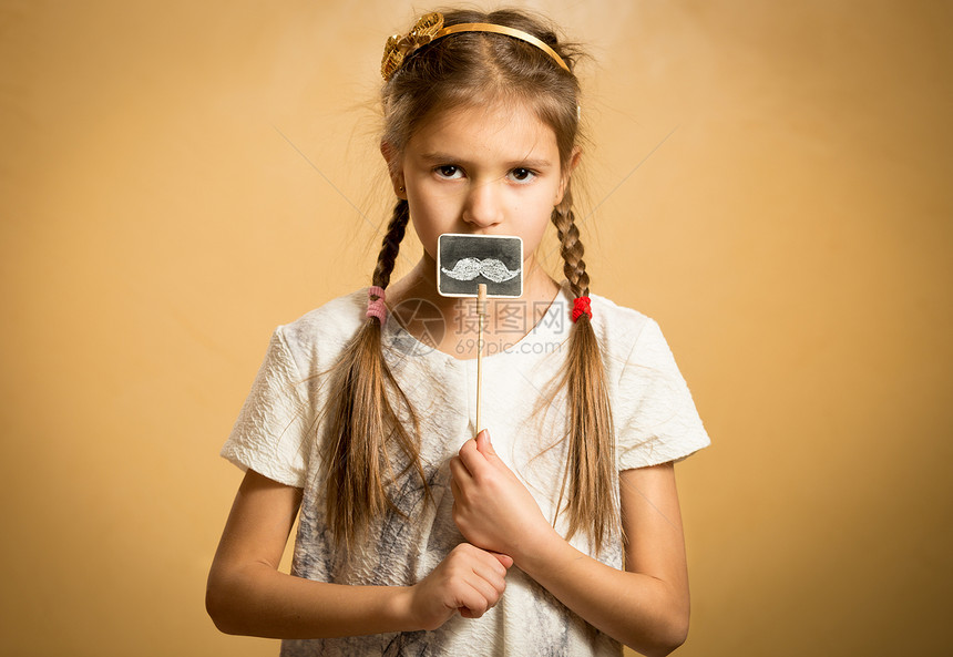 可爱的小女孩拿着有趣的装饰胡子图片