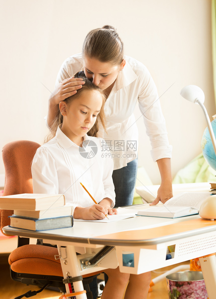 年轻母亲在做家庭作业时拥抱和赞扬女儿的肖像图片