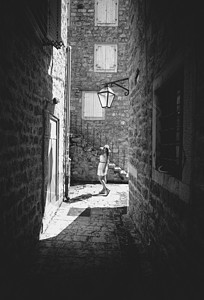 古代妇性年轻女在旧窄街上行走的黑白照片背景