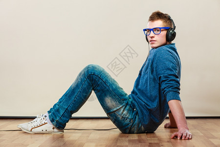 年轻时装男耳机坐在地板上听音乐年轻的高清图片素材
