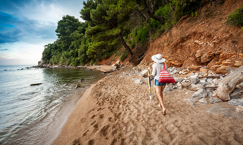 美丽的年轻女背着包袋走在废弃的海边图片