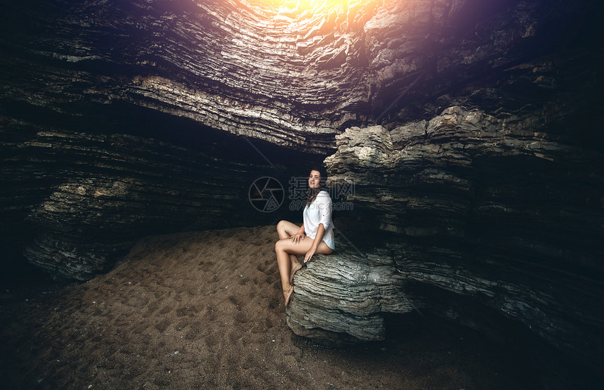 美丽的年轻女士坐在悬崖上日落的光下在壁橱的上图片