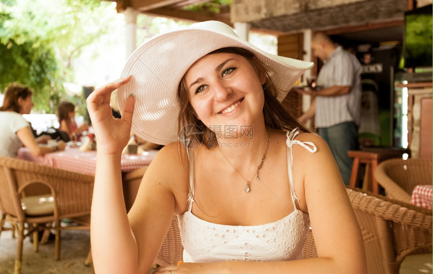 在阳光明媚的日子坐在咖啡厅里着戴白帽子的可爱笑女人肖像图片