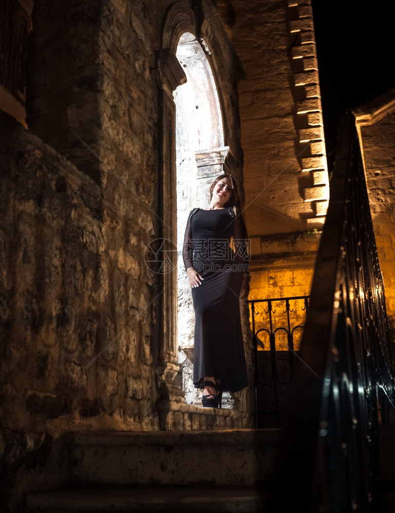 穿着长裙的感瘦女人晚上靠着旧石拱门图片