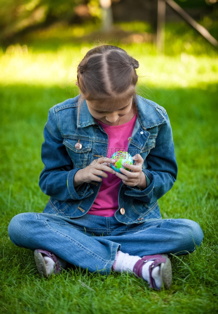 坐在公园草地上探索球的小女孩图片