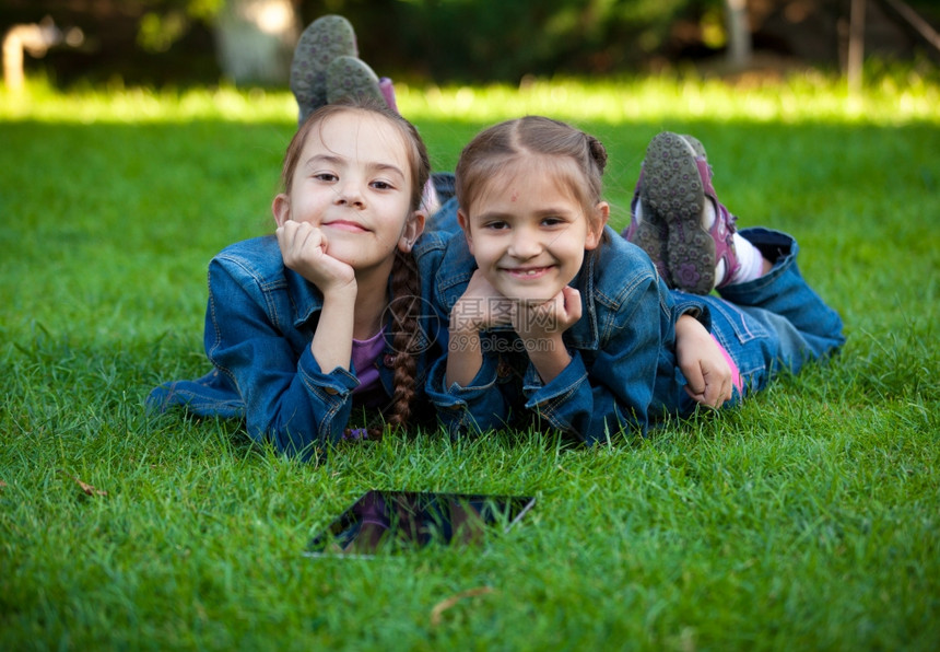 两名小女孩用平板电脑躺在草地上的近距离肖像图片