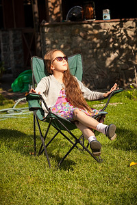 美丽的年轻女孩在阳光明媚的白天在草地上坐椅子放松舒适的高清图片素材