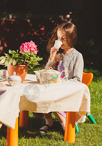 美丽的可爱女孩在院子里的玩具桌边喝茶吃高清图片素材