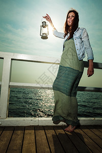 海灯全长的年轻女子在码头配有油煤灯概念上携带光亮日背景