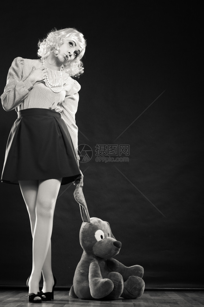 年轻女孩穿着木偶娃和大狗玩具站在黑白相片旁图片