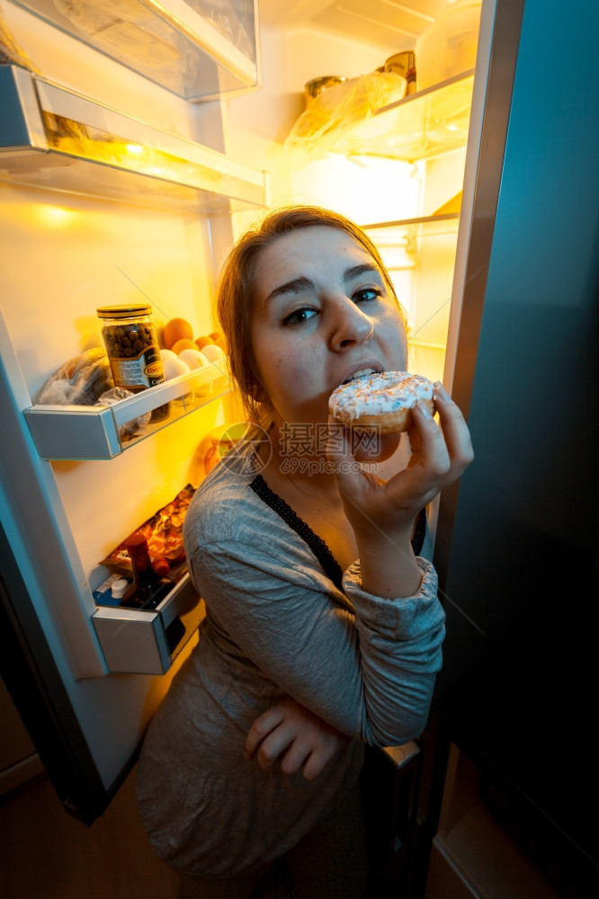 女人晚上在露天冰箱附近咬甜圈的近镜头肖像图片