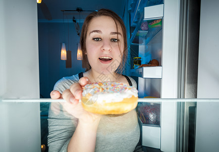 年轻女子晚上从冰箱里拿出甜圈的近视肖像图片
