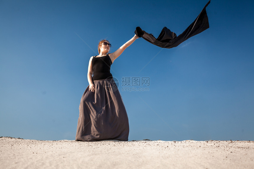 长着裙的漂亮女人穿着黑色布站在沙丘上图片