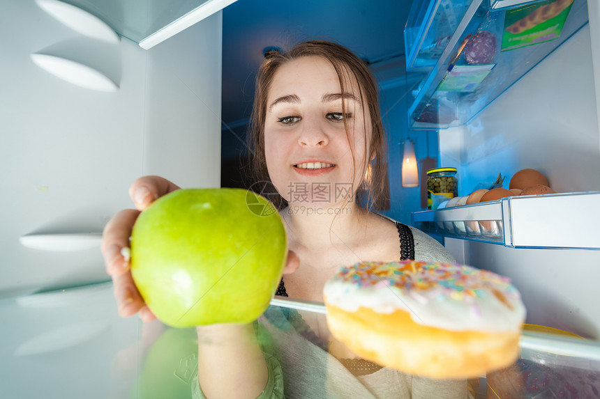 女人吃绿苹果的冰箱里肖像图片