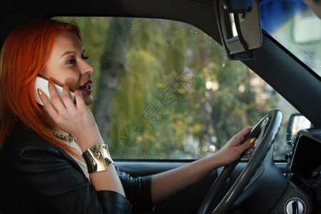 年轻女司机红发孩在开车时用手机智能电话说背景图片