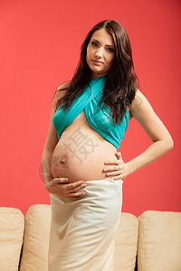 怀孕母亲和幸福概念穿着围巾的有吸引力孕妇在红色背景下触摸肚子图片