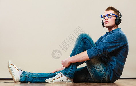 年轻时装男耳机坐在地板上听音乐男性的高清图片素材