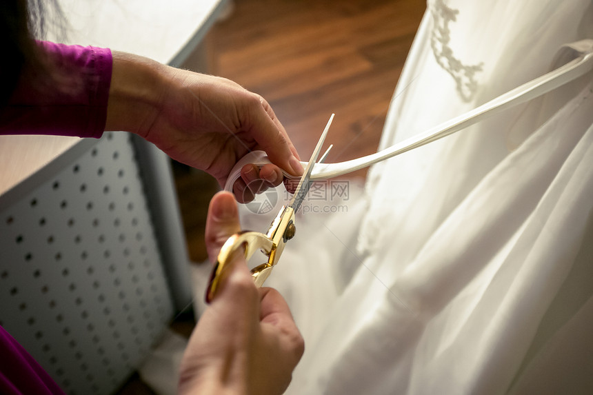 裁缝剪的近身镜头脱下白色婚纱的丝带图片