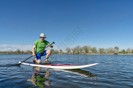 时尚的老人在平静的湖中间跪在皮划桨上划水背景图片