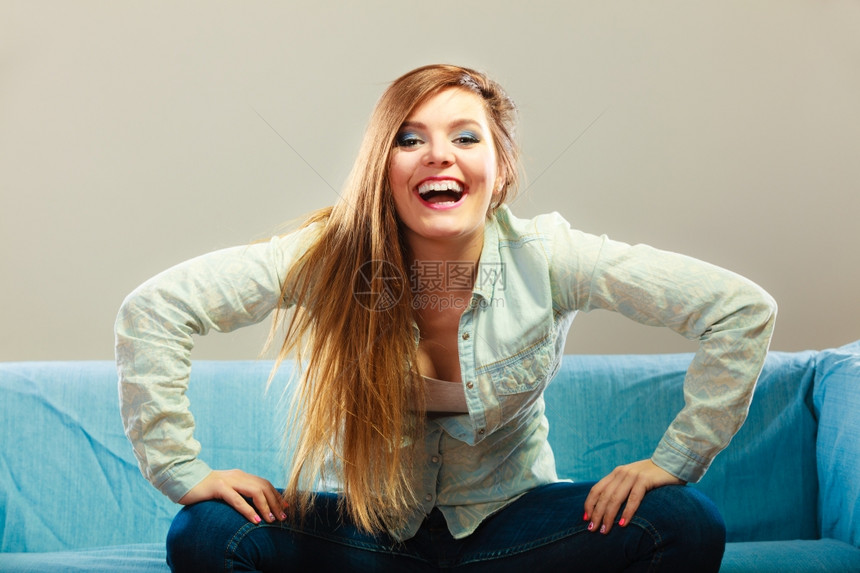 青年幸福概念轻时装的快乐女孩坐在蓝沙发上身着牛仔服坐在蓝沙发上图片