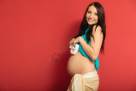 怀孕母亲和幸福概念孕妇为红背景未出生婴儿穿小鞋靴的孕妇背景图片