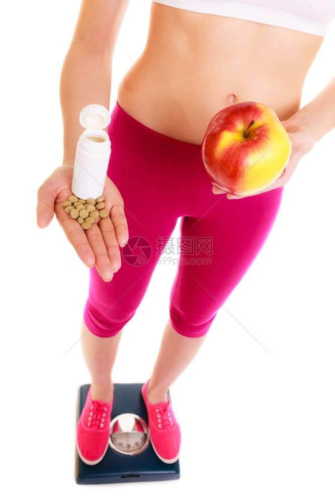 年轻女站在持有药丸和苹果的称号上在合成维生素之间做出选择保健康生活方式营养概念白种背景孤立图片