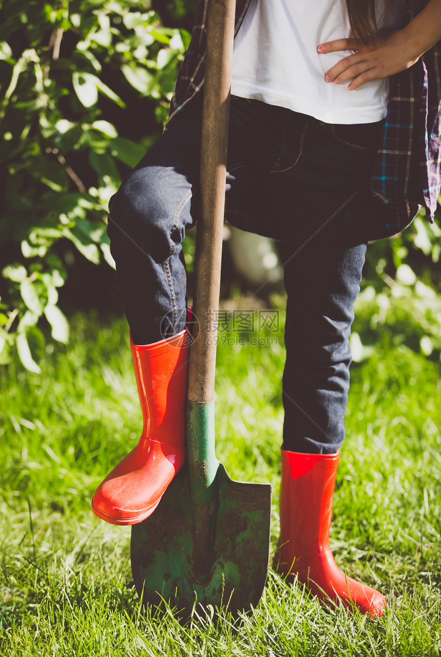 在花园铲子上用橡皮靴绑着腿的年轻女子近贴照片图片