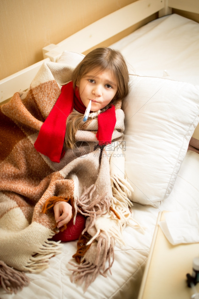 穿着泰迪熊和测量温度躺在床上的可爱生病女孩肖像图片