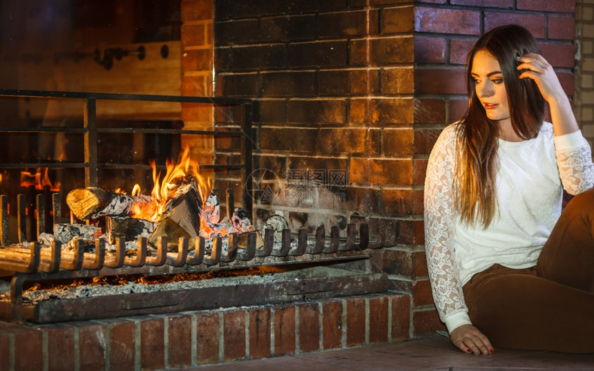 在壁炉里休息 冬之家忧郁的女人在壁炉里休息 怀念着旧的年轻女孩暖和起来 家里冬天图片