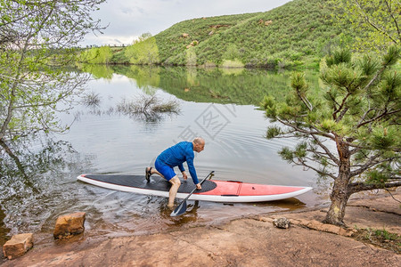 高级男护工在湖边岩石岸霍赛牙储藏室科林斯堡罗拉多推出红色SUP滑板图片