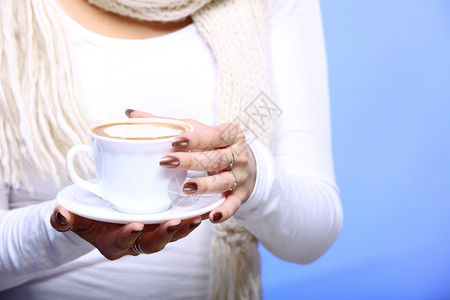女近身手紧拿着一杯铁咖啡卡布奇诺热饮在冬季蓝色背景拿铁高清图片素材
