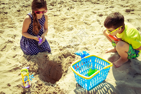 带铲子的小女孩和男儿在沙滩上玩得开心背景图片