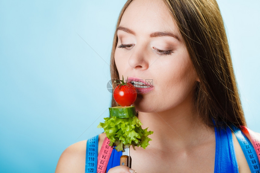 健美保和减肥概念运动健壮的女子身妇颈部有测量带在蓝底有叉子新鲜混合蔬菜工作室拍摄图片