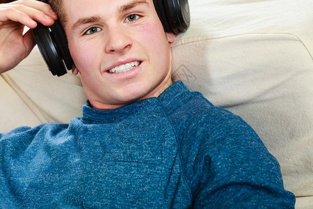 英俊的年轻人带着耳机躺在沙发上家里听音乐音乐的高清图片素材