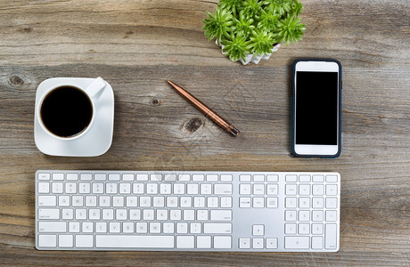 顶端是整齐的桌面键盘黑咖啡绿色植物和手机在木制桌上图片